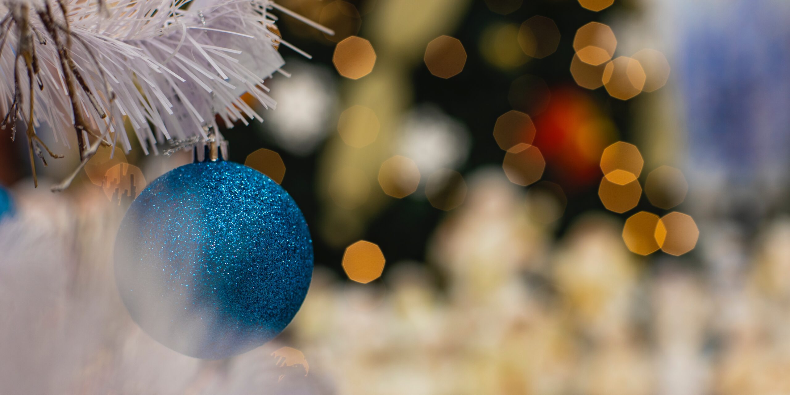 Blue ornament with white garland against blurred Christmas lights