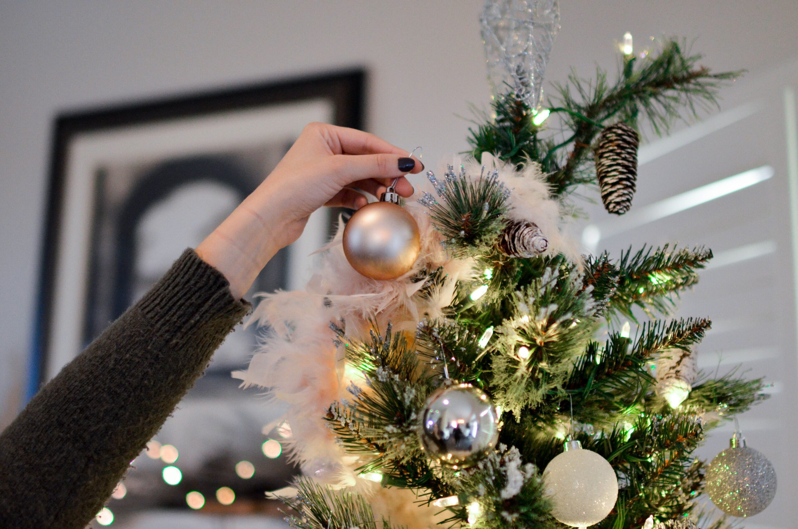 Woman’s hand putting an ornament on a white, tan & green Christmas tree